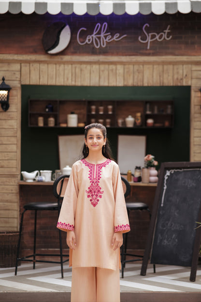 Lily girl wearing a peach kurta and trouser set with magenta floral embroidery and mirror work at a cafe setting