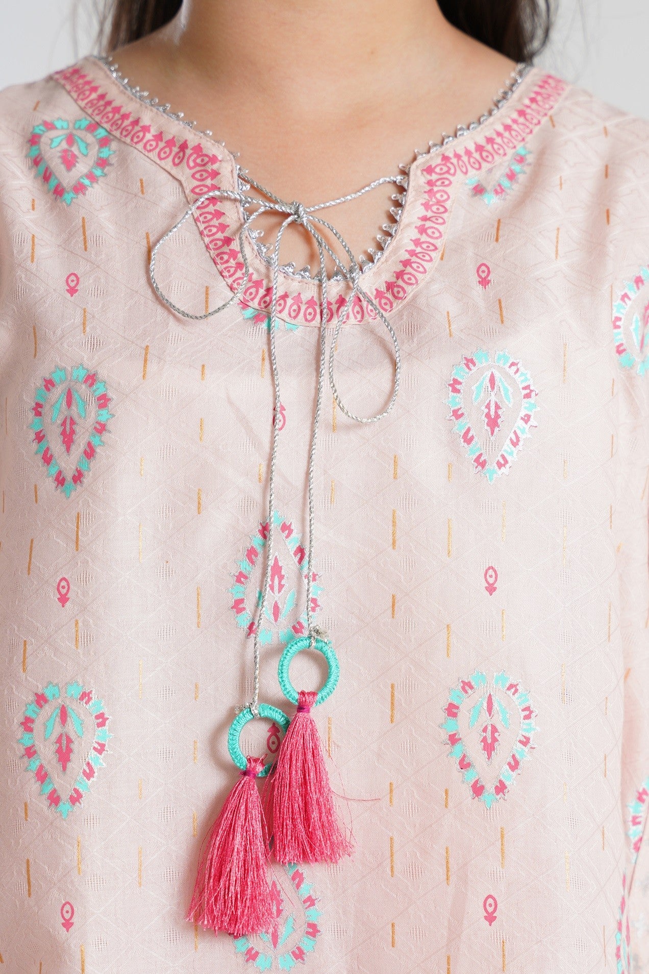 Lily pink embroidered tunic with teal and gold print, V-neck, silver trim, and pink tassels. Paired with palazzo pants.