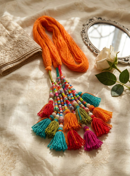Lily Satrangi Beads Paranda featuring a vibrant orange yarn base with multi-colored beads and festive tassels.