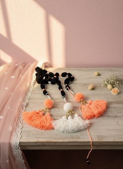 Lily handcrafted coral, white, and black yarn hair accessory with pom-poms and gold beads.