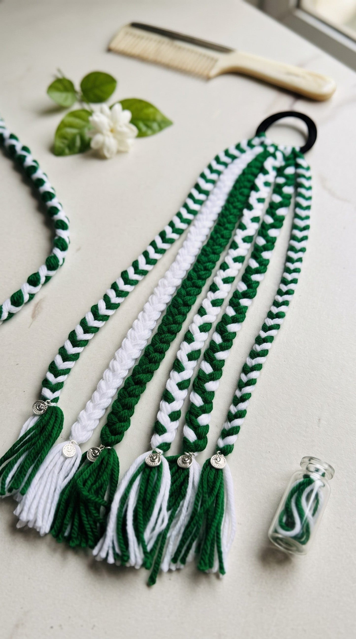 Lily Watan Love braided hair accessory with green and white yarn strands, metallic charms, and a black hair tie.
