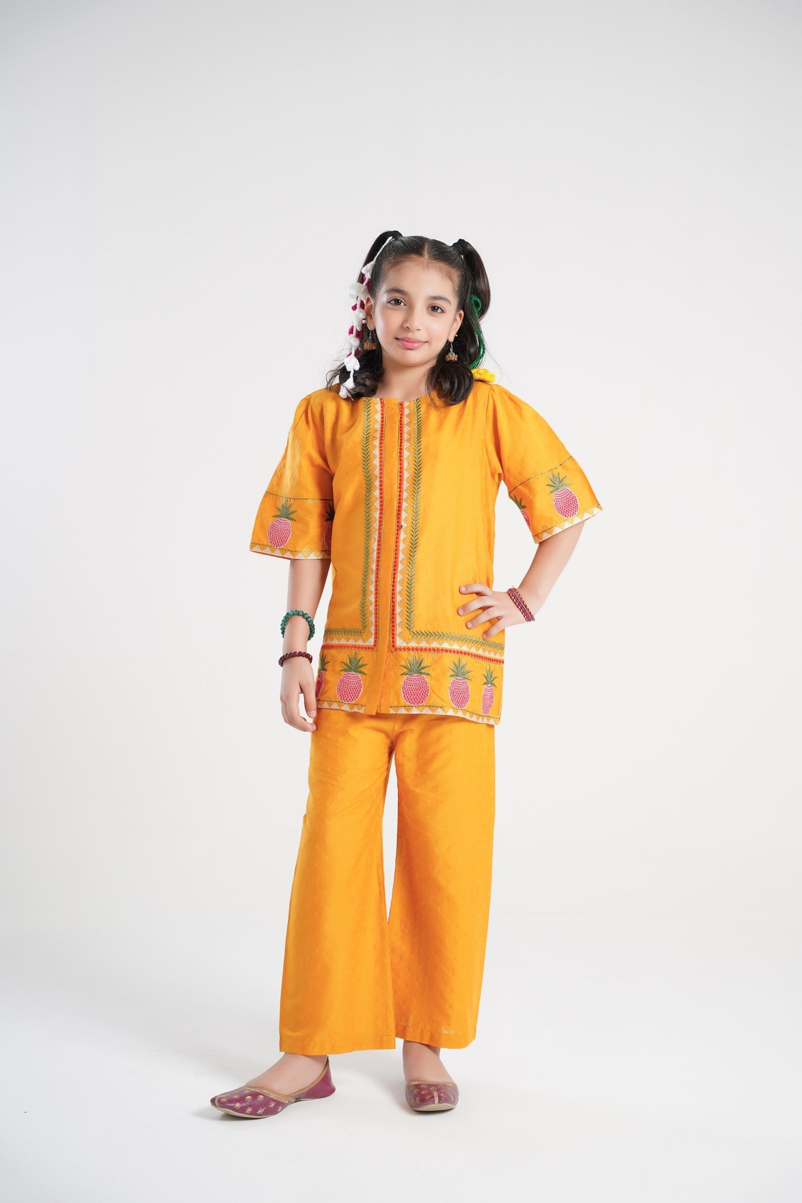 Lily yellow textured cotton kurta and pants set with pineapple embroidery and green/red trim. Girl model with pigtails.