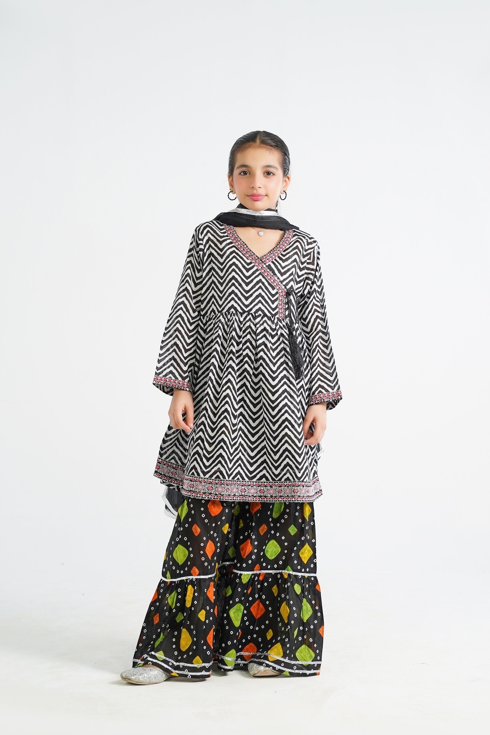 Lily black and white zigzag print kurta with red embroidery and tassels, paired with colorful tiered sharara and dupatta.