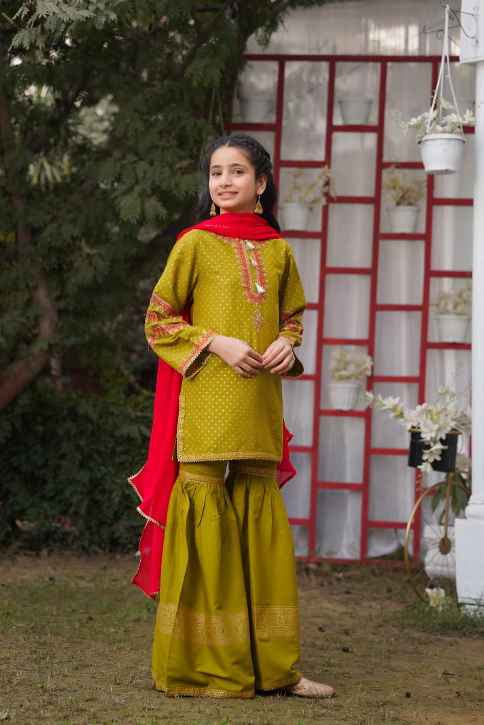 Young girl in a green traditional outfit with a red dupatta standing outdoors.